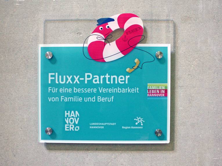 Das Schild "Fluxx-Partner" zeigt einen Rettungsring mit einem Telefonh&ouml;rer und wird an Betriebe vergeben, die sich an der Notfall-Kinderbetreuung Fluxx beteiligen.