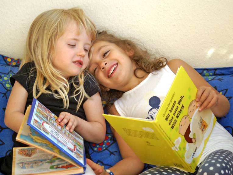 Zwei Kinder sitzen nebeneinander und schauen sich Bücher an