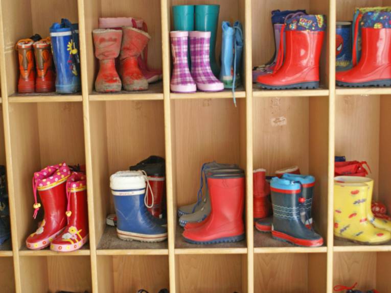 In einem Holzregal stehen Gummistiefel von Kindern