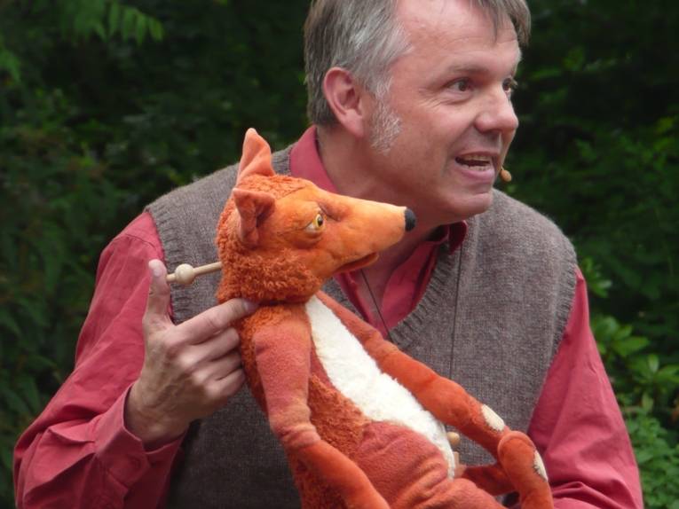 Ein Puppenspieler mit einem Fuchs als Stockhandpuppe