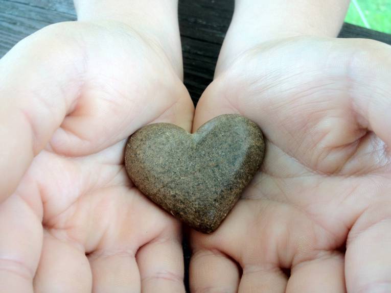 Stein in Herzform wird von zwei Händen getragen