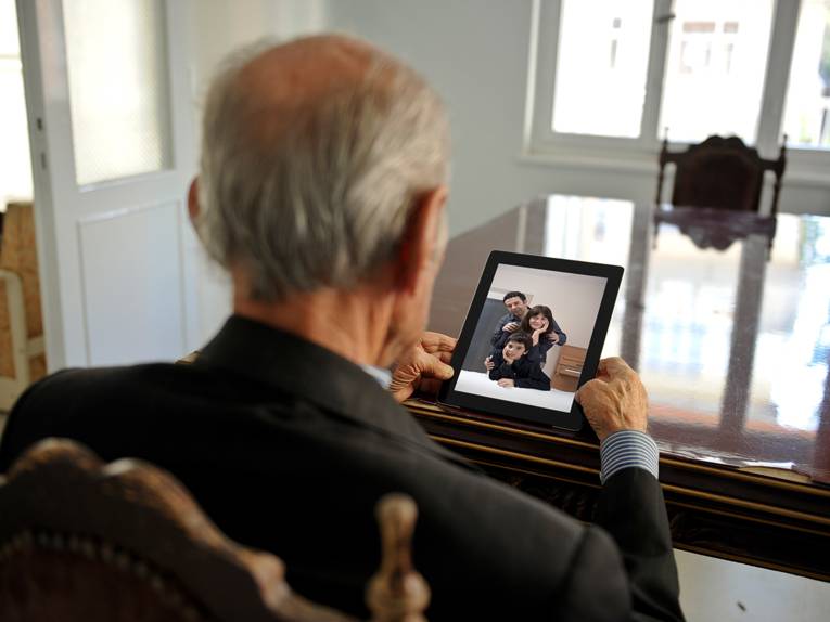 Ein alter Herr betrachtet allein an einem Tisch sitzend ein Familienfoto.