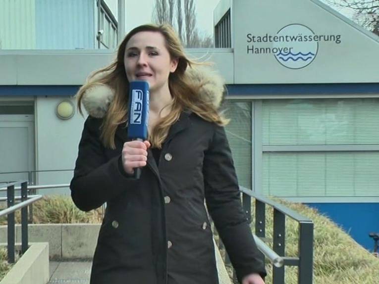 FAN-Moderatorin Aileen Noeske steht mit Mikrophon vor der Stadtentwässerung Hannover