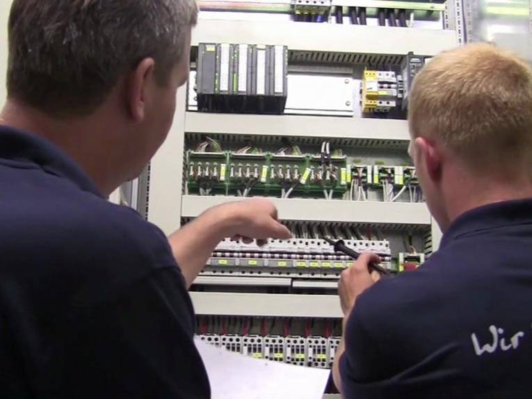 Elektroniker-Azubi und Ausbilder vor Schaltschrank