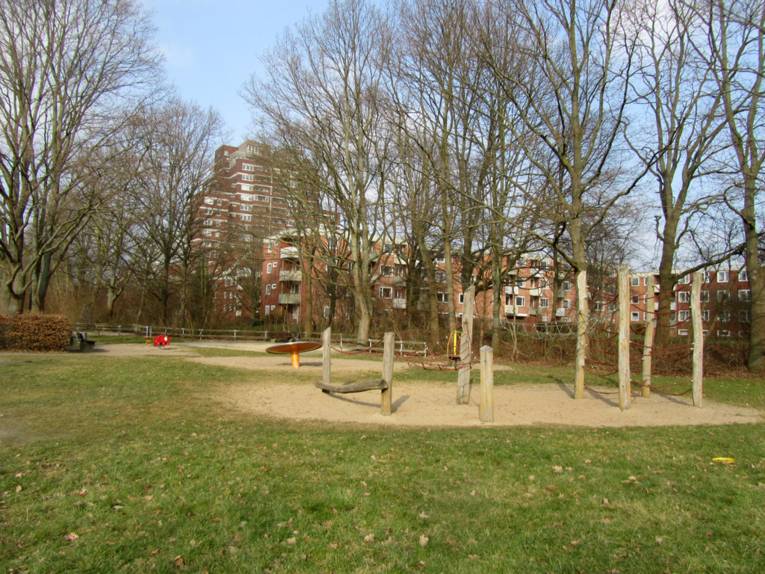 Spielplatz mit Klettergerüst, Wippschaukel und Drehteller vor Wohnsiedlung