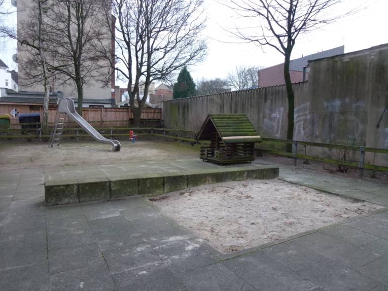 Rutsche und Holzhäuschen auf betonierten Spielplätz mit zwei Sandkästen