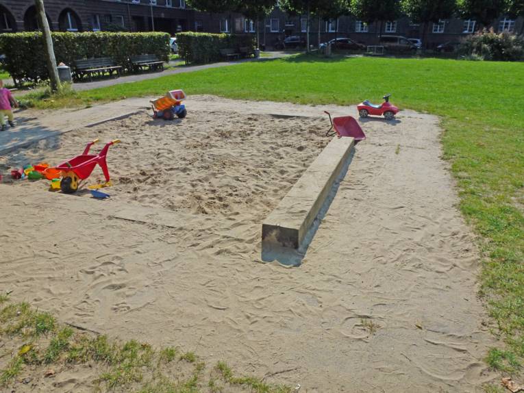 Spielplatz mit Sandkiste und Rasenfläche. 