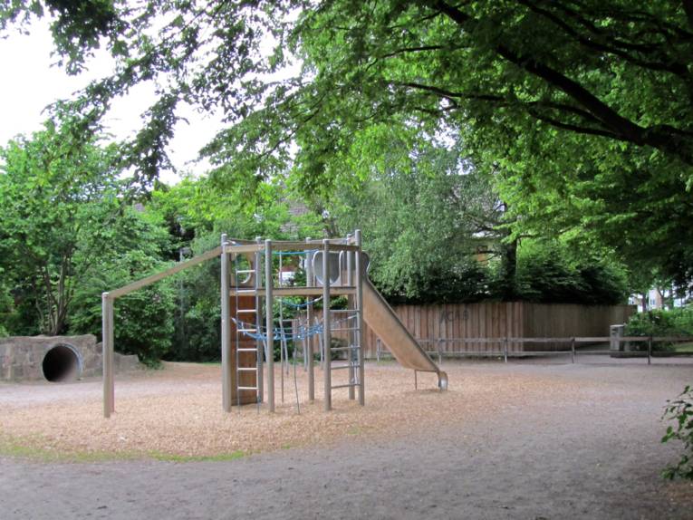 Ein Klettergerüst mit Rutsche unter Bäumen auf dem Spielplatz Schollweg