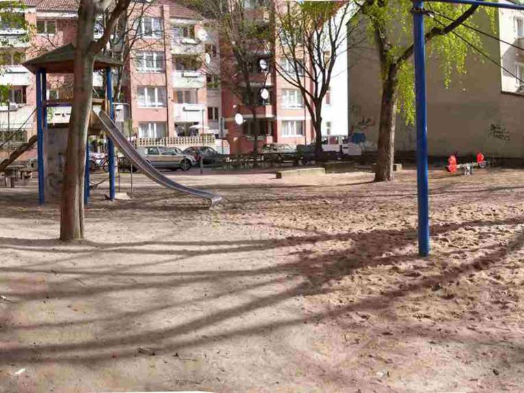 Spielplatz mit Rutsche und Wippe, im Hintergrund Mietshäuser