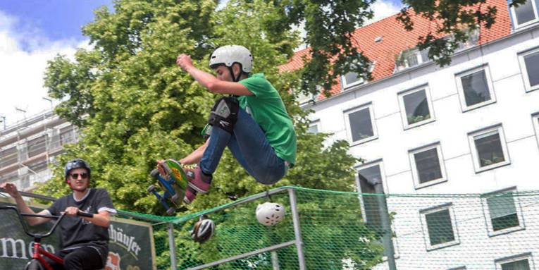 Ein junger Skater mit Helm und Knieschützern in der Luft auf seinem Skateboard