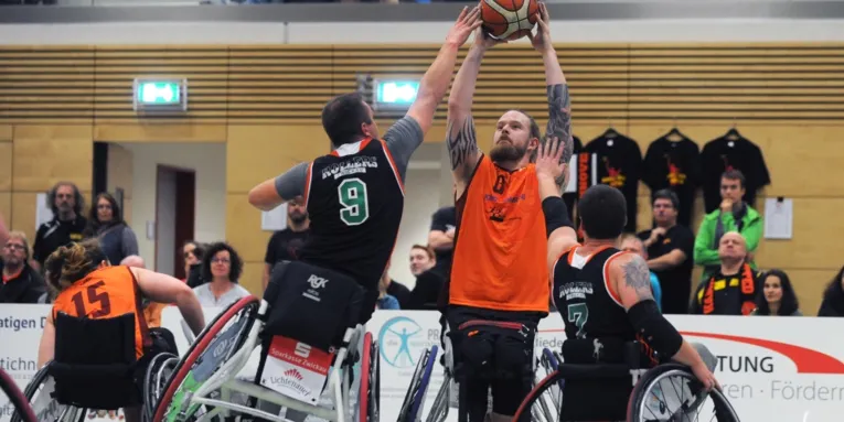 Beim Rollstuhlbasketball kämpfen vier Spieler um den Ball.