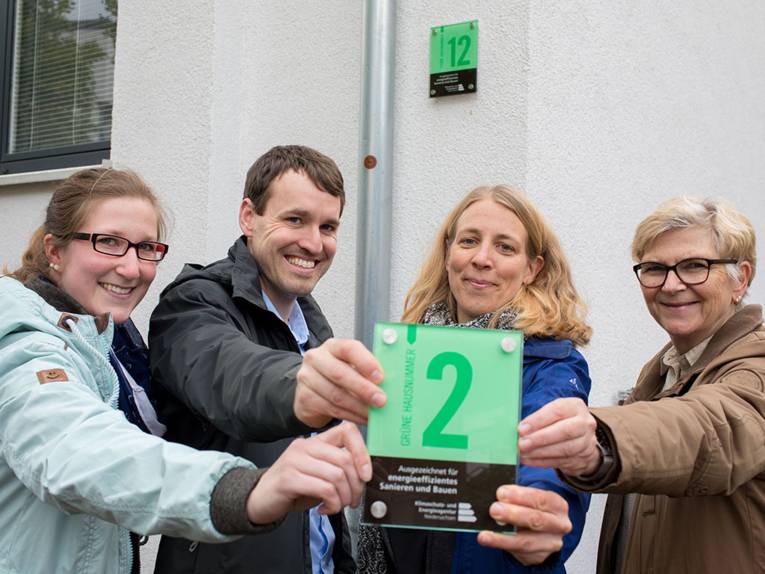 Vier Personen halten eine grüne Hausnummer in die Kamera.