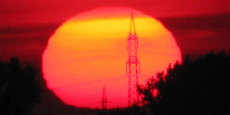 Die Sonne geht auf und erleuchtet einen Strommasten