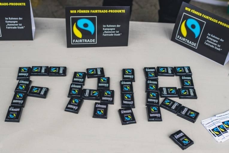  Auf einem Tisch bilden kleine Schokoladentäfelchen mit Fairtrade-Logo das Wort Fair