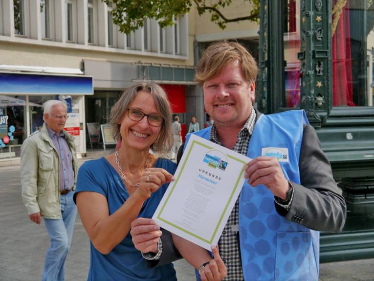Susanne Wildermann vom Agenda21- und Nachhaltigkeitsbüro und Carsten Elkmann von TransFair e.V.  präsentieren am Kröpke die Fair Trade Town Urkunde für Hannover