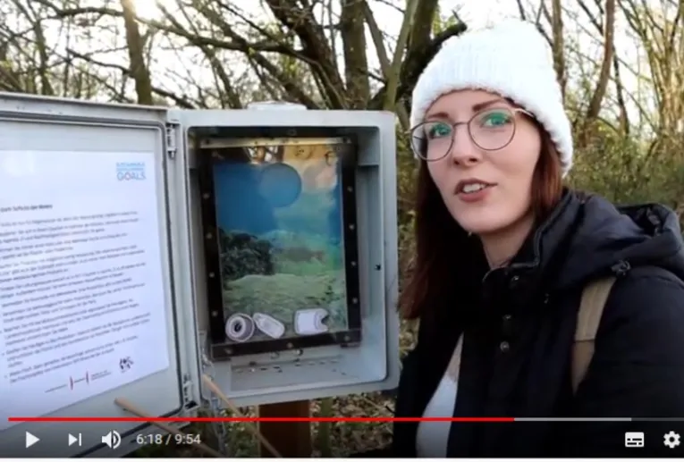 Eine junge Frau steht vor einem geöffneten Cache zum Thema "Leben im Wasser"