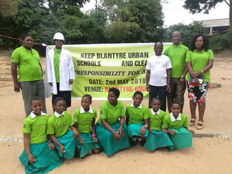 Gruppenbild mit Organisatorinnen und Organisatoren, Schulkindern und dem stellvertretendne Bürgermeister der Stadt Blantyre vor einem Plakat.