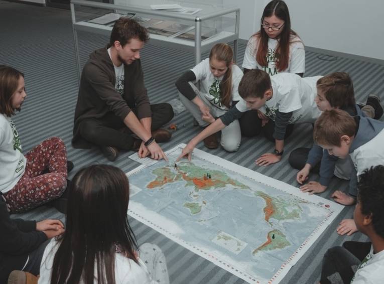 Kinder sitzen beim Weltspiel um eine große Weltkarte