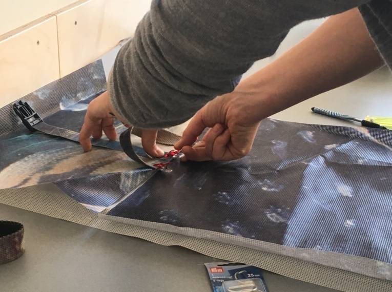Eine Person näht aus alten Bannern einen Rucksack.