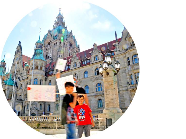 Zwei Kinder und ein Mann halten Schilder vor dem Neuen Rathaus hoch.
