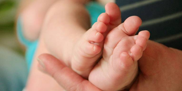 Füße eines Babys in der Hand eines Erwachsenen.