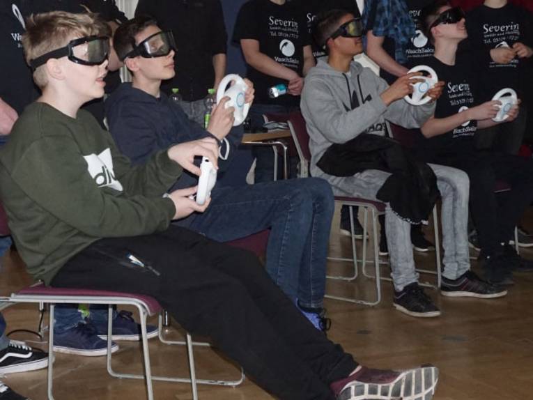 Kinder und Jugendliche, die mit einer speziellen Brille ein Videospiel spielen. 