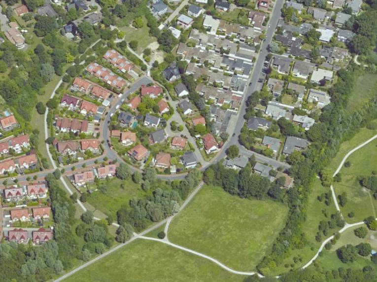 Luftbild mit Sicht auf Ein- und Mehrfamilienhäuser, die von städtischem Grün (Felder und Bäume) umrahmt sind.