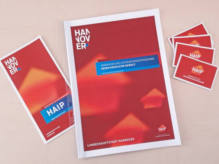 Ein Flyer, Postkarten und der Jahresbericht des Hannoverschen Interventionsprogramms gegen Häusliche Gewalt liegen auf einem Tisch.