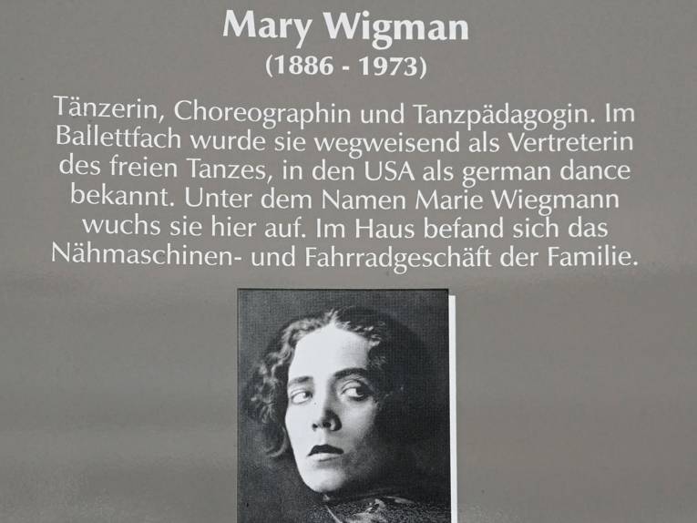Ausschnitt aus einer Gedenktafel zu Mary Wigman, die ein Portraitfoto einer jungen Frau mit großen Augen zeigt, und biografische Daten auflistet.