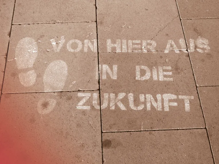 Auf einem gepflasterten Weg sind zwei Fußabdrücke aufgebracht, daneben der Schriftzug "Von hier aus in die Zukunft".
