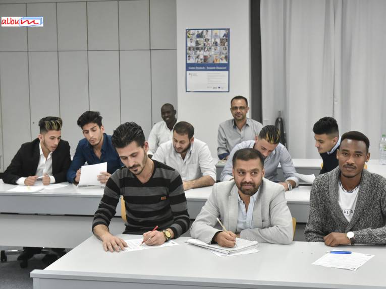 Zehn junge Männer sitzen an Tischen in einem Unterrichtsraum und lösen Aufgaben.
