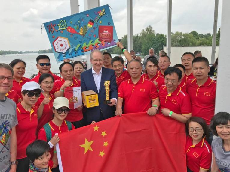 Oberbürgermeister Stefan Schostok inmitten eines Teams von Sportlern am Maschsee. Die Sportlerinnen und Sportler präsentieren die chinesische Fahne.