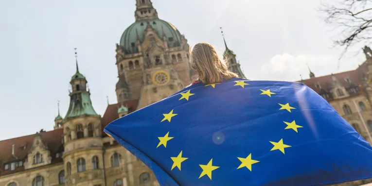 Eine Person steht vor dem Neuen Rathaus und hält eine große Europafahne hoch.