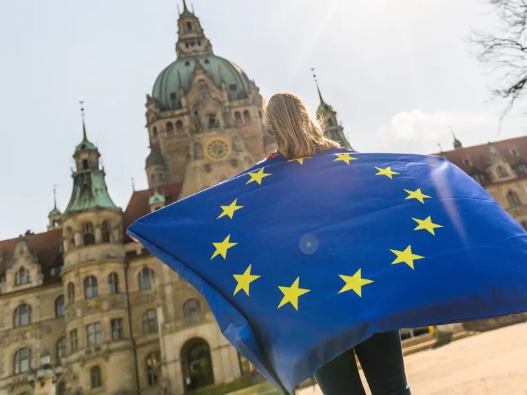 Eine Person steht vor dem Neuen Rathaus und hält eine große Europafahne hoch.