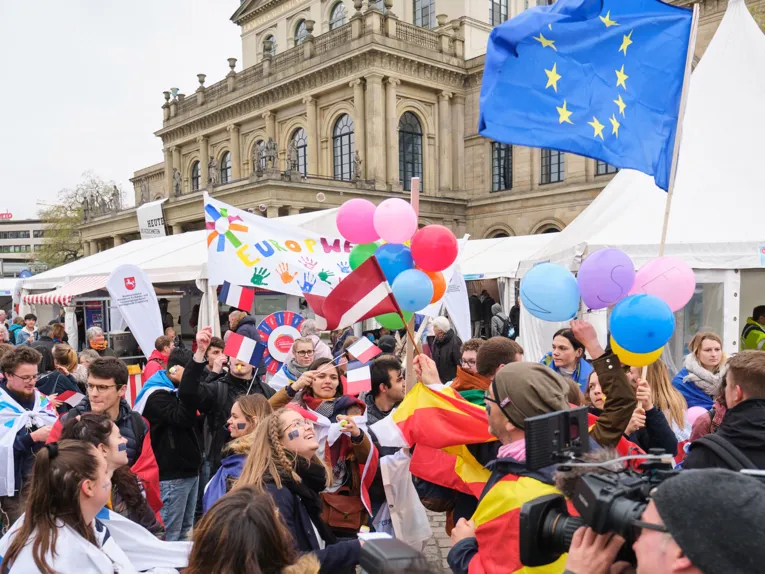 Eine bunte Menschenmenge steht vor der Oper, eine Europafahne wird geschwenkt. 