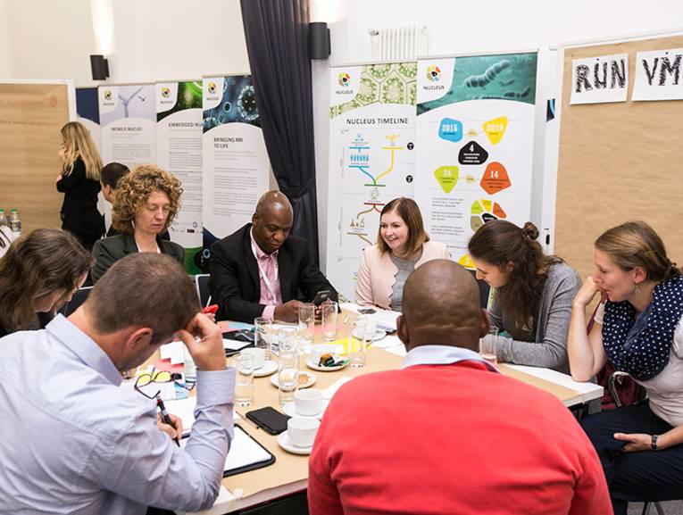 Eine Gruppe Personen sitzt um einen Tisch mit Dokumenten und scheint sich zu unterhalten.