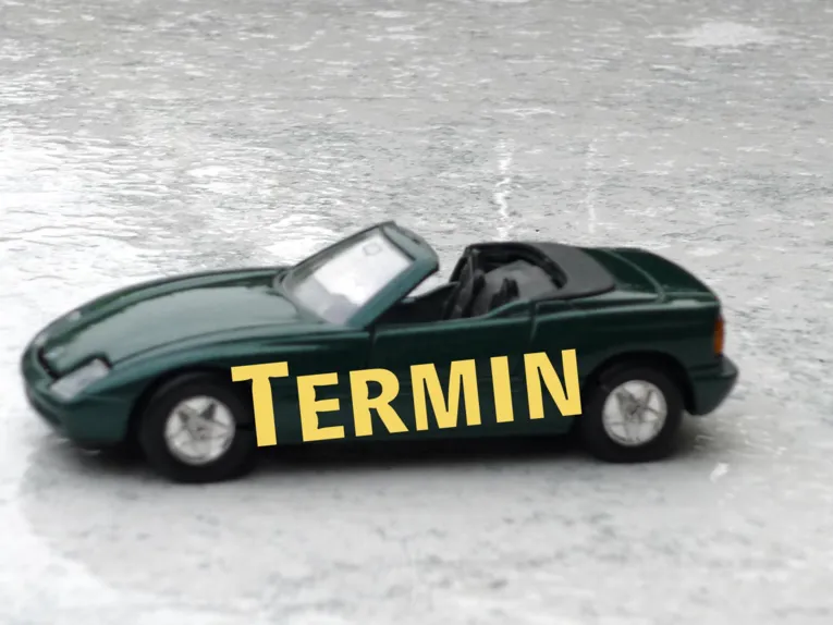 Grüner Wagen mit Seitenbeschriftung "Termin" auf regennaßem Untergrund