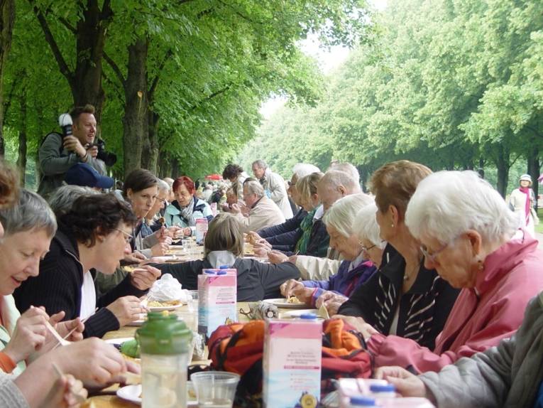 Junge und alte Menschen sitzen gemeinsam zum Essen an einer langen Tafel in der Herrenhäuser Allee