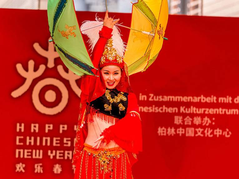 Chinesische Tänzerin in rotem Kostüm jongliert mehrere Sonnenschirme auf einer Bühne