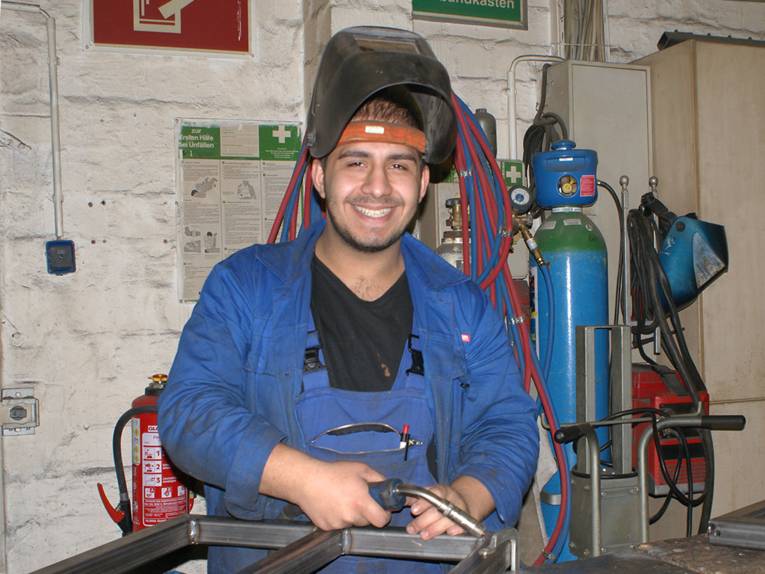 Ein angehender Metallbauer in Arbeits- und Schutzkleidung mit einem Schweißgerät in der Ausbildungsstätte