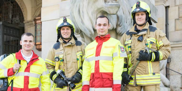 Zwei Auszubildende zum Notfallsanitäter und zwei Auszubildende für den Feuerwehrtechnischen Dienst mit ihrer Arbeitsausrüstung