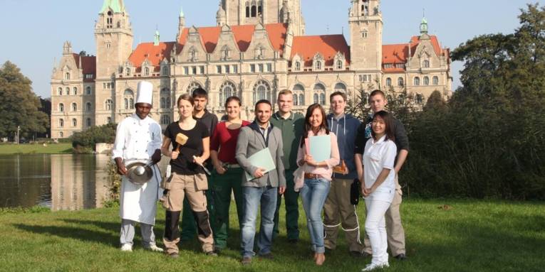 Zehn Auszubildende - zum Teil in Berufskleidung - aufgereiht vor dem Neuen Rathaus in Hannover