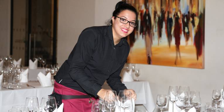 Junge Frau in Berufskleidung beim Eindecken eines Tisches im Restaurant "Der Gartensaal"