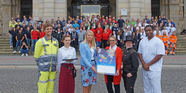 Eine große Personengruppe steht vor dem Neuen Rathaus Hannover in diverser Berufsbekleidung mit einem Plakat, das für die "Lange Nacht der Berufe" wirbt.