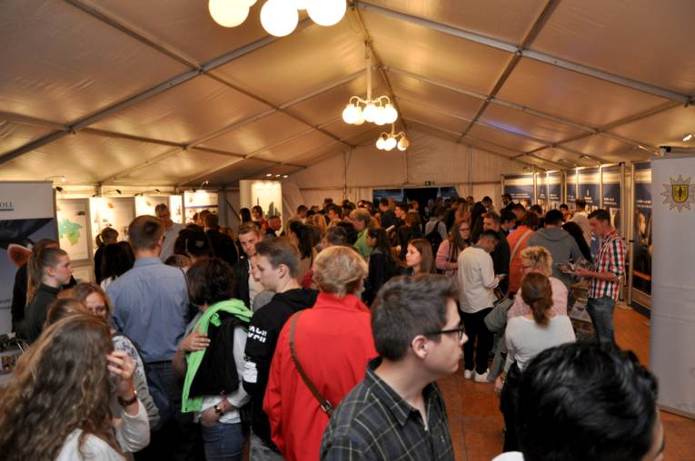 Menschen, die sich in einem Zelt verschiedene Stände ansehen. 