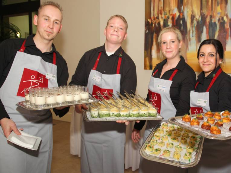 Vier Gastronomie-Servicekräfte mit Tabletts, auf denen vegetarisches Essen steht