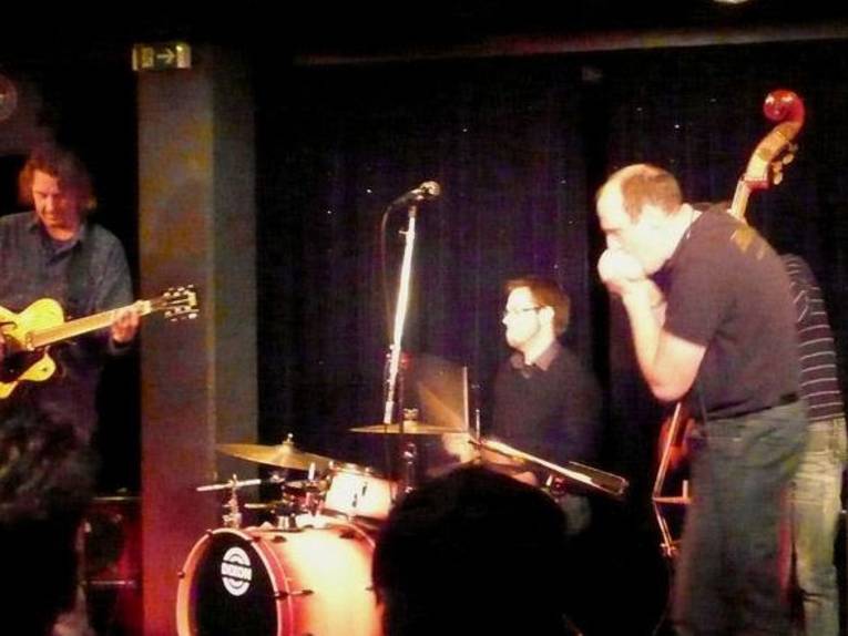 Drei Männer mit Instrumenten auf einer Bühne.