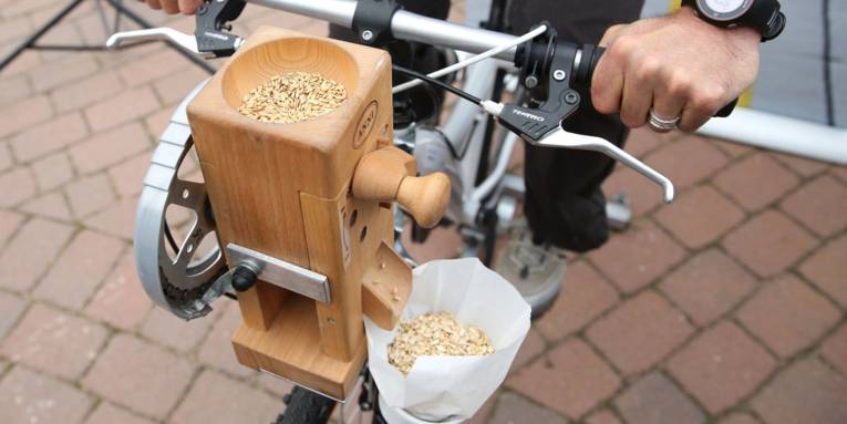 Fahrrad, an dem eine Getreidemühle befestigt ist.