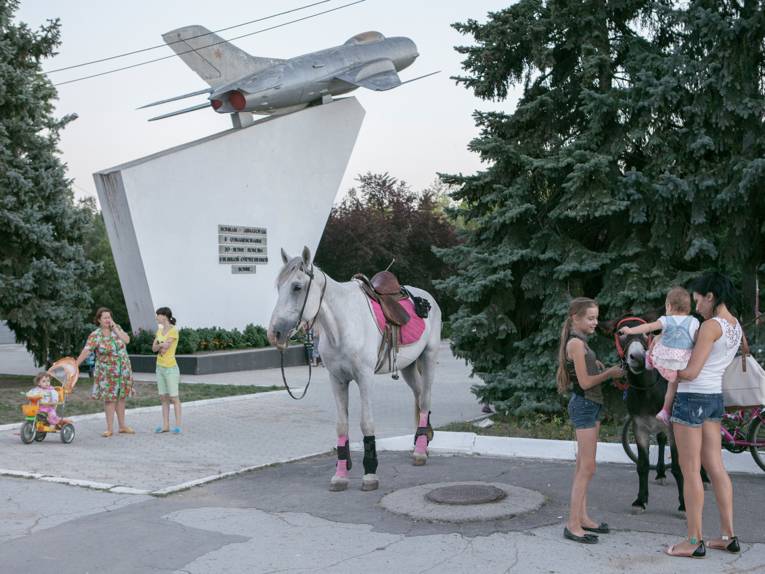 Frauen mit Kindern und einem Pferd vor einem Jagdflieger-Denkmal. 