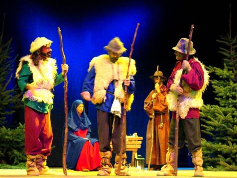 Eine Bühne mit drei Hirten, Maria, Josef und einer Krippe zwischen Weihnachtsbäumen.